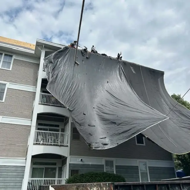 Large protective tarp hoisted over the roof edge of a four-story building