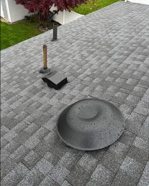 Plumbing vent pipe and a round roof vent on a gray asphalt shingle roof