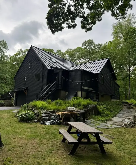 Black standing-seam metal roof on a dark two-story home surrounded by trees