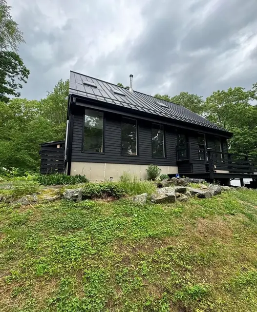 Black standing-seam metal roof on a dark-sided house above a grassy slope