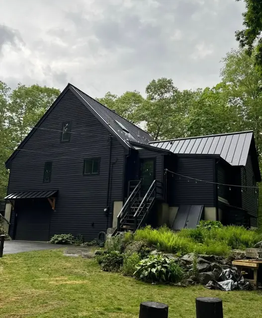 Black standing-seam metal roof on a dark-sided house with a stone retaining wall