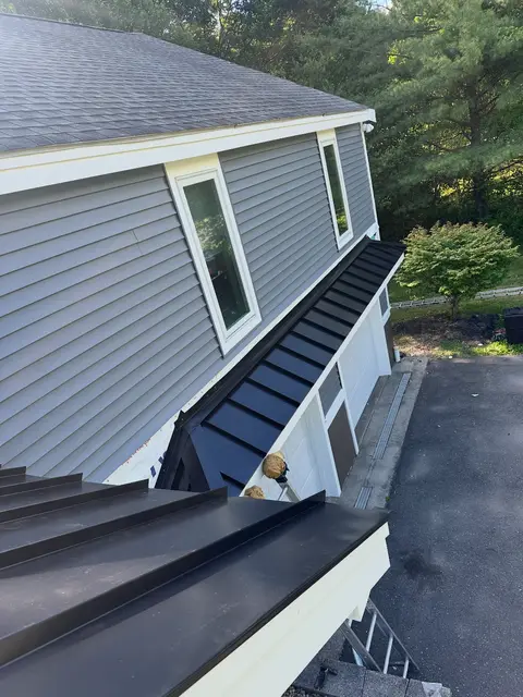 Black standing-seam metal porch roof below gray vinyl siding, seen from above