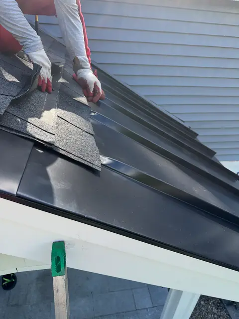 Gloved hands fitting shingles where they meet a black standing-seam porch roof