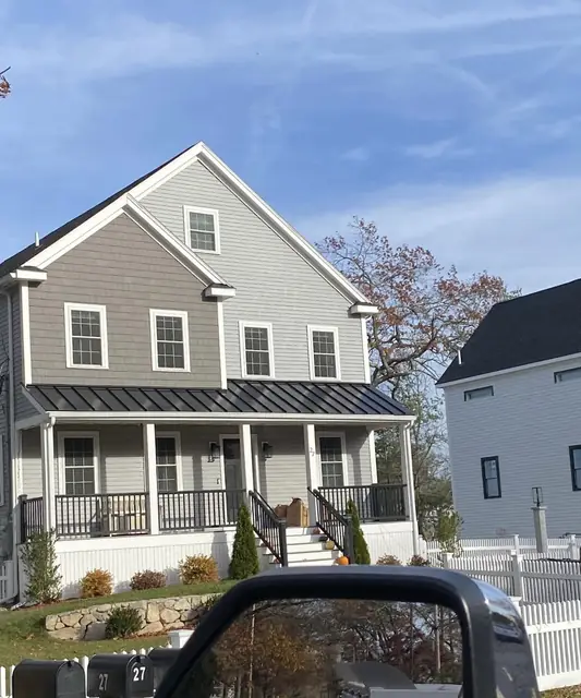 Dark standing-seam metal roof over the front porch of a gray two-story colonial